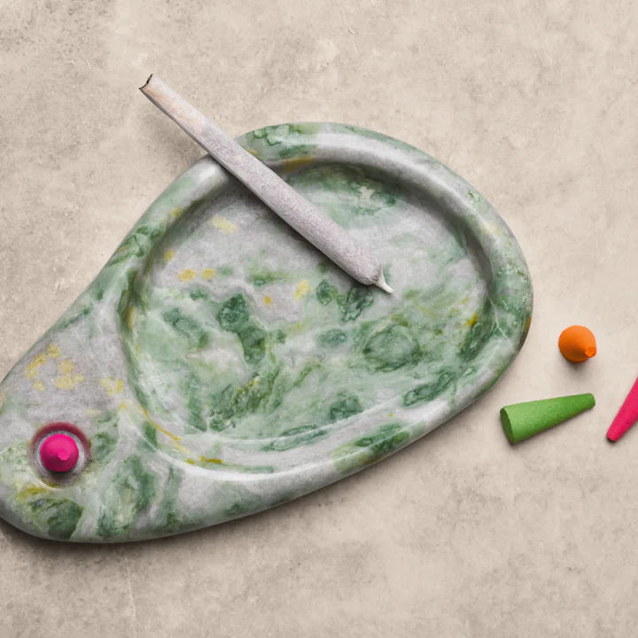 Marble-patterned smoking accessory with colorful incense cones on a beige surface